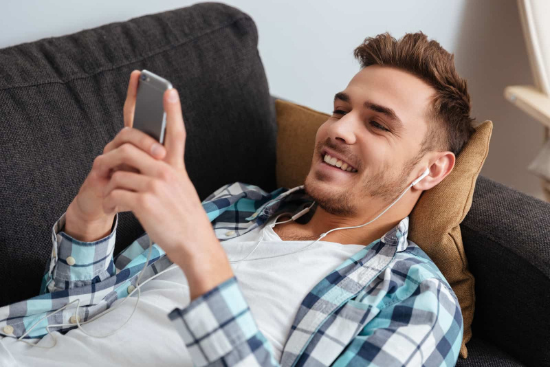   homem deitado no sofá e olhando para o telefone