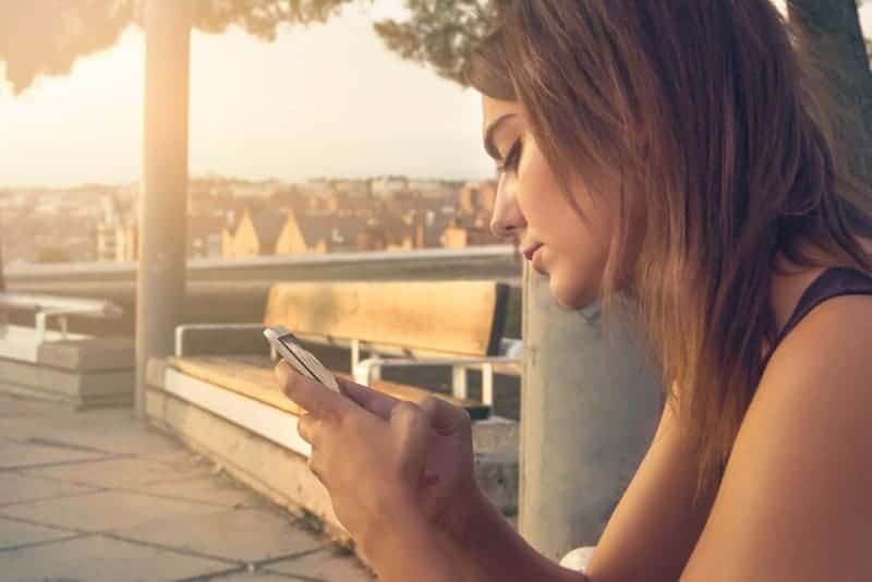 dona escrivint al seu telèfon asseguda fora