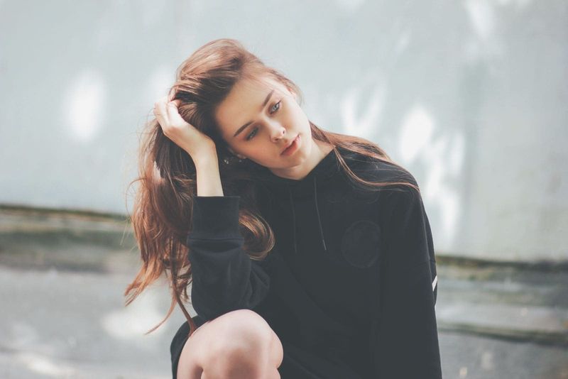 kobieta w dużym kapturze, siedząca zamyślona na zewnątrz z ręką dotykającą jej głowy