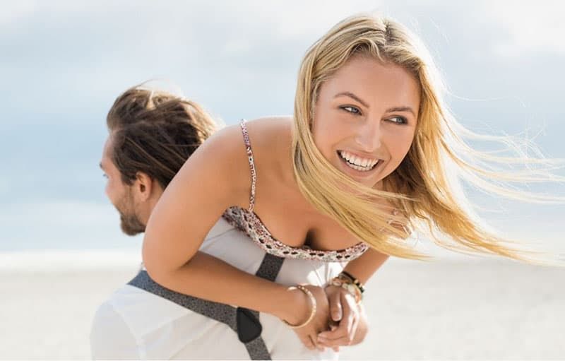 portret młodej szczęśliwej pary cieszącej się na świeżym powietrzu, gdzie mężczyzna piggybacking kobietę na plaży